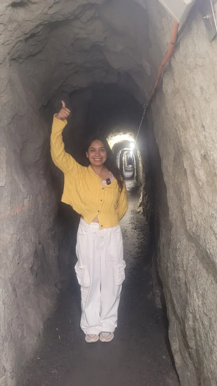 Traveler Jyoti inside the Urnerloch — a narrow rock-cut tunnel with daylight visible at the far end
