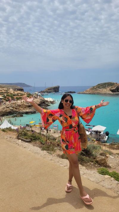 Traveler Jyoti with her arms open at the turquoise Blue Lagoon, Comino, Malta