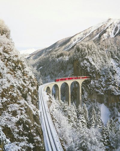 Red Swiss alpine train passing through snow-capped mountains — must-have travel apps for Europe