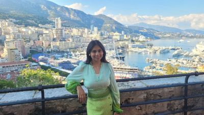 Traveler Jyoti on a terrace high above Monaco, with the superyacht harbour of Port Hercules, the city and the mountains behind her