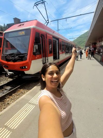 Traveler Jyoti taking a selfie on a station platform with a red regional train behind her