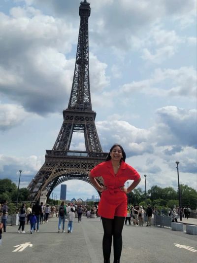 Traveler Jyoti in a red dress standing in front of the full Eiffel Tower in Paris