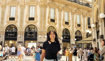 Traveler Jyoti inside the Galleria Vittorio Emanuele II arcade in Milan, with Prada storefronts and the ornate gallery behind her
