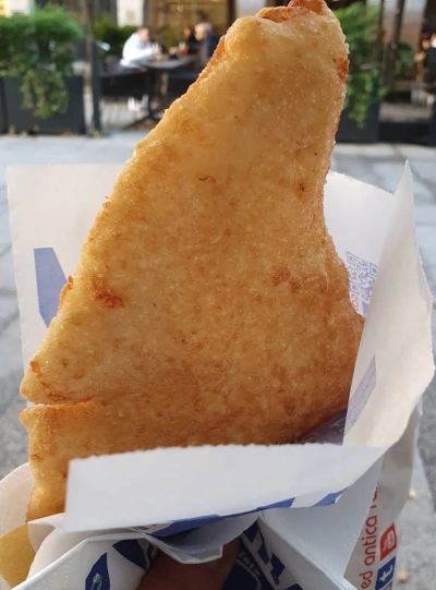 A golden deep-fried pizza fritta in a paper wrap on a Milan street, looking just like an Indian bhatura