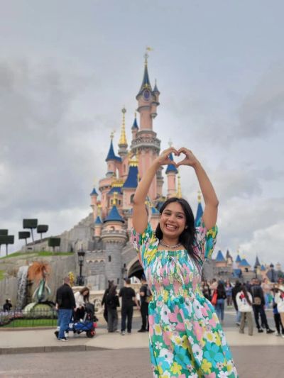 Traveler Jyoti making a heart with her hands in front of the Sleeping Beauty castle at Disneyland Paris