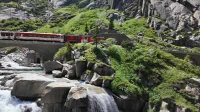 A red Swiss regional train crossing a stone bridge over a rushing mountain river gorge