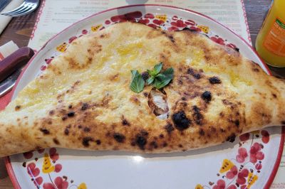 A folded baked calzone topped with basil on a decorative plate at Pizzium in Milan