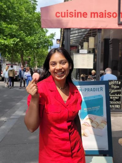 Traveler Jyoti holding a pink French macaron outside a Paris patisserie