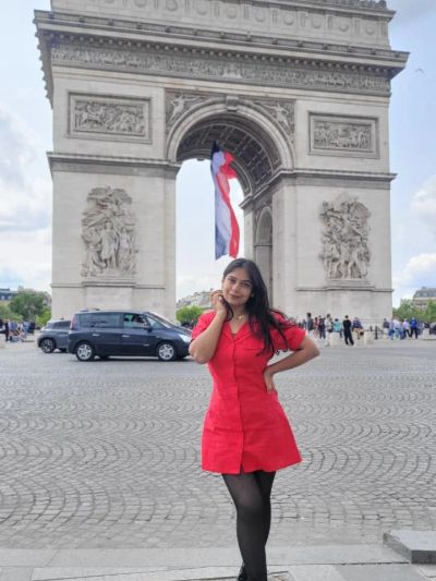 Traveler Jyoti in a red dress in front of the Arc de Triomphe with the French flag