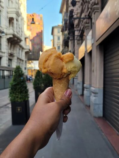 A gelato cone with two scoops held up on a Milan street