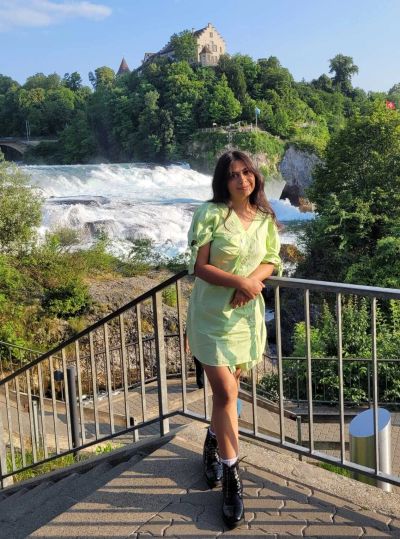 Traveler Jyoti standing on the free Neuhausen platform with Schloss Laufen castle on the cliff across the river