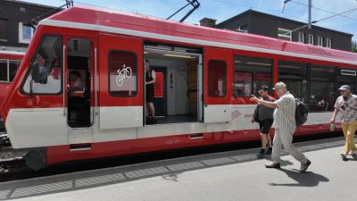 A red Matterhorn Gotthard Bahn regional train at a Swiss station with its doors open