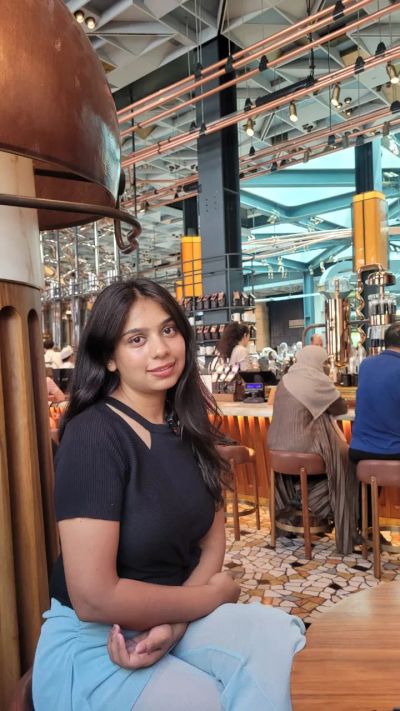 Traveler Jyoti sitting inside the Starbucks Reserve Roastery in Milan beside the copper coffee-roasting machines