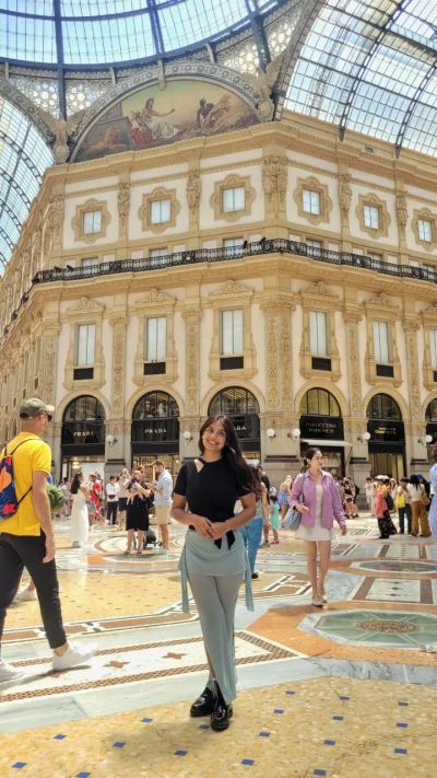 Traveler Jyoti standing inside the Galleria Vittorio Emanuele II arcade in Milan with luxury storefronts behind her