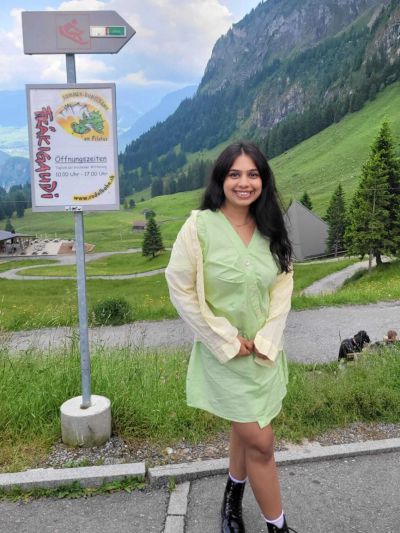 Traveler Jyoti next to the Fräkigaudi summer toboggan run sign at Fräkmüntegg showing opening hours 10:00 to 17:00